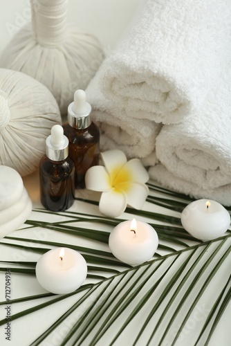 Composition with different spa products, burning candles and plumeria flower on white table
