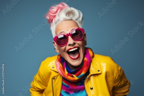 Funny senior woman with pink hair and sunglasses on blue background.