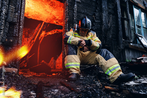 Concept psychological injury and burnout at work after loss of team, death of people from incidents. Sad fireman sits next to burning house, hard profession of rescue services