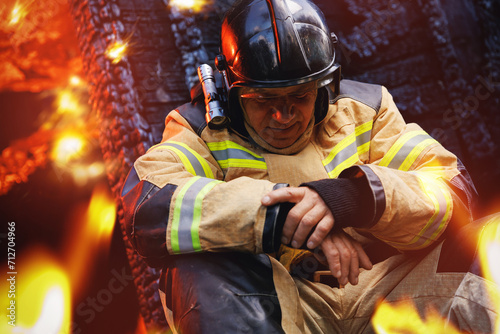 Canvas-taulu Sad fireman sits next to burning house, hard profession of rescue services