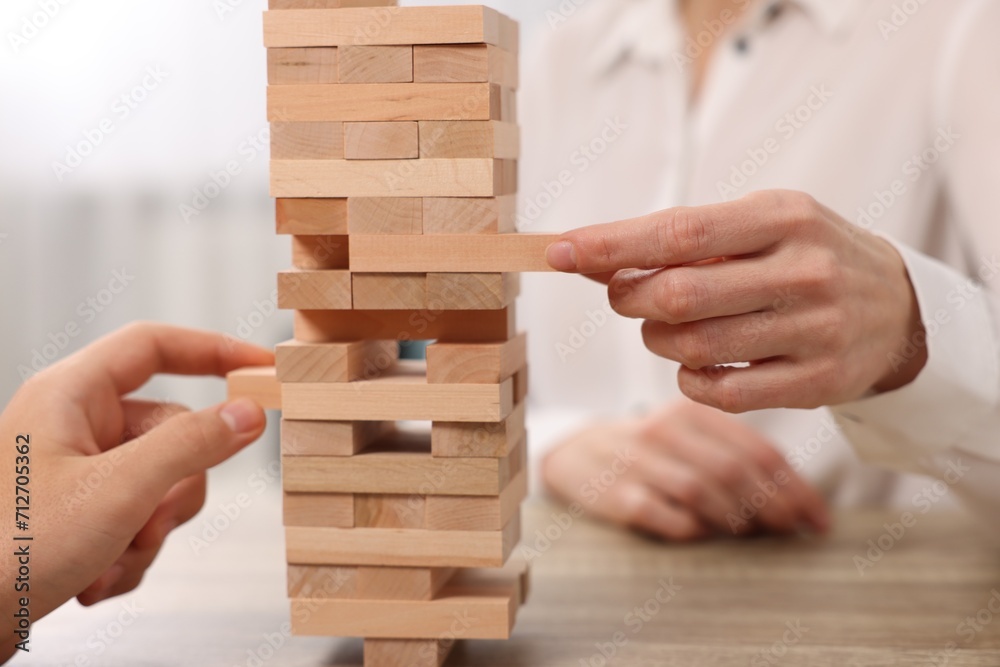 People playing Jenga tower at wooden table indoors, closeup People playing Jenga tower at wooden table indoors, closeup