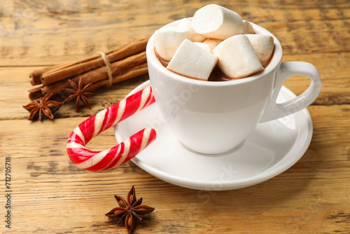 Tasty hot chocolate with marshmallows, candy cane and spices on wooden table, closeup
