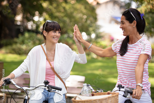 two women high five with bicycle at park