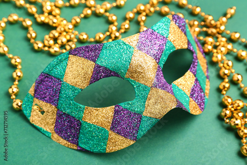 Shiny carnival mask with beads for Mardi Gras celebration on green background