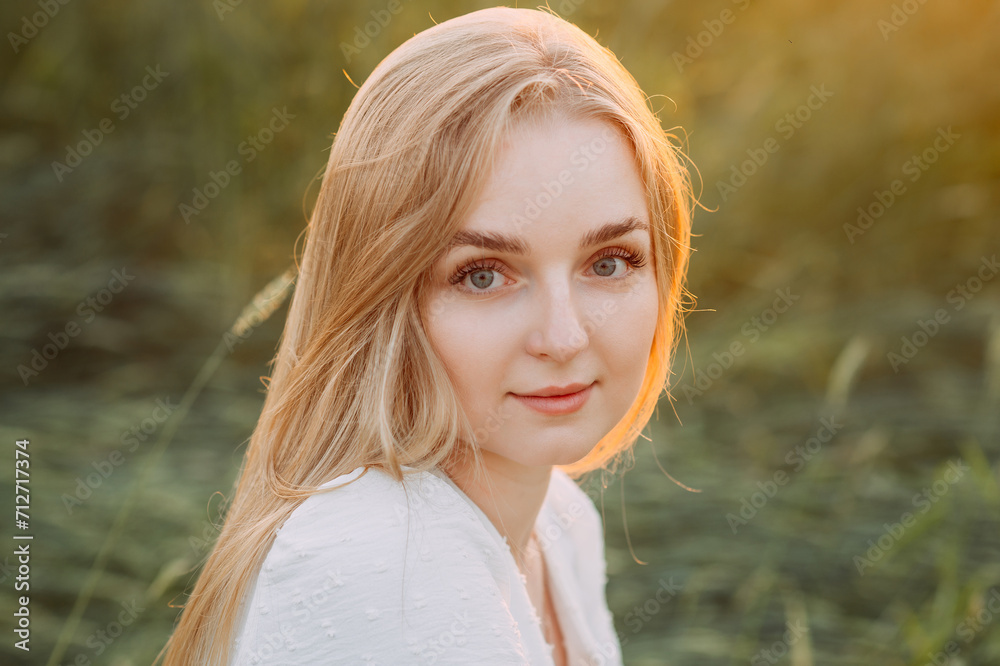 Naklejka premium A woman with blonde hair smiling in an outdoor setting, possibly a grassy field 5737.