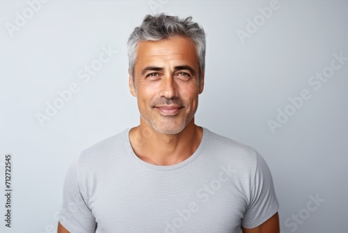 Portrait of handsome mature man with grey hair looking at camera and smiling while standing against grey background photo