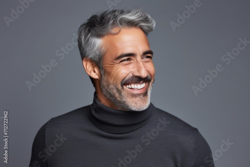 Handsome middle-aged man in a black turtleneck and smiling at the camera while standing against grey background