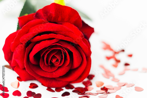 rosa rossa circondata da confetti rossi a forma di cuore su sfondo bianco a san valentino photo
