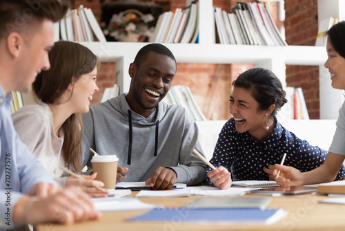 Smiling international young people sit at desk have fun studying preparing group project together  happy overjoyed multiethnic students laugh joke working in team cooperating or brainstorming in class