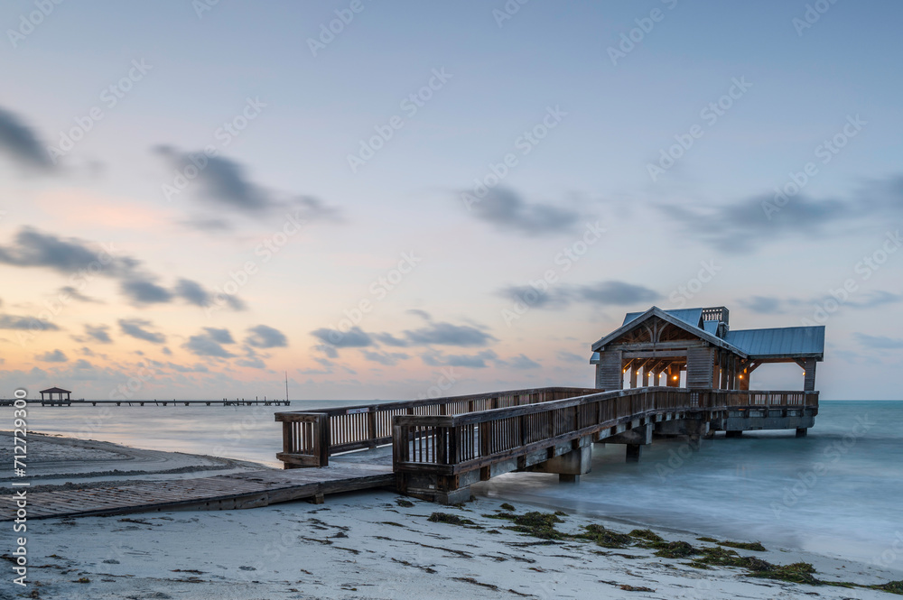A wooden pier or jetty, reaching out into a calm ocean, at sunrise, as colour creeps into the sky.