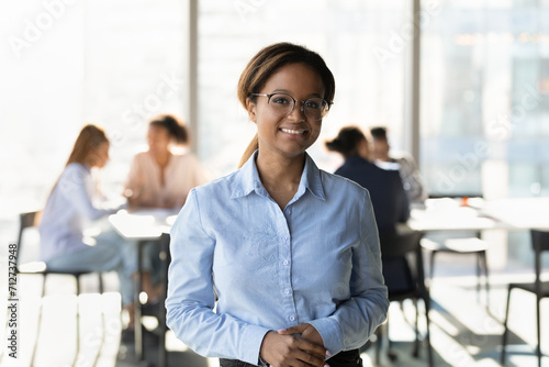 Portrait of happy millennial mixed race businesswoman professional manager consultant wearing glasses formal shirt. Friendly young lady receptionist look at camera meet client at bank corporate office photo