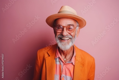 Portrait of a happy senior man in hat and glasses on pink background