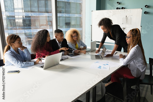 At negotiating table. Two mixed race females managers present financial report on pc screen to diverse partners group. Young women startupers convince possible investors in business project benefits