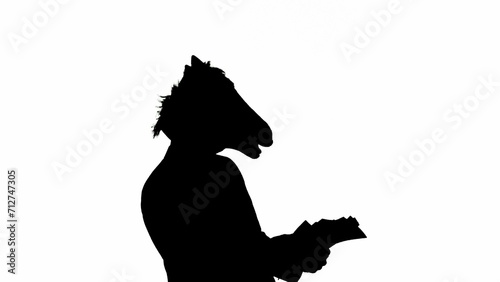 Black silhouette of man in business suit with horse head mask on white isolated studio background. A businessman is looking through documants. Concept of hard office work. photo