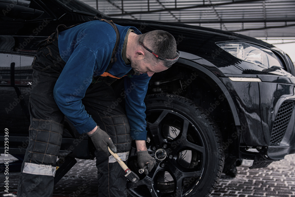 Mechanic at a service station in overalls repairs a wheel on a car.