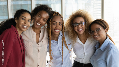 United with common goal. Happy friendly multiethnic female staff of accounting office bank department hug look at camera. Group portrait of young biracial women colleagues team enjoy working together photo