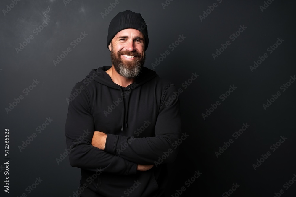 Bearded man in black hoodie and hat with crossed arms on black background Bearded man in black hoodie and hat with crossed arms on black background