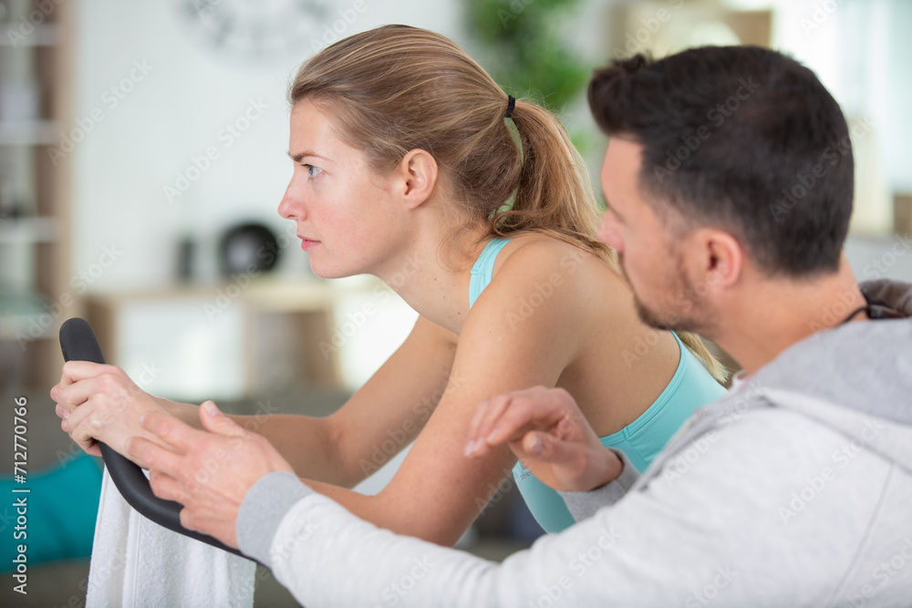 Fototapeta premium focused woman uses exercise machine encouraged by personal trainer