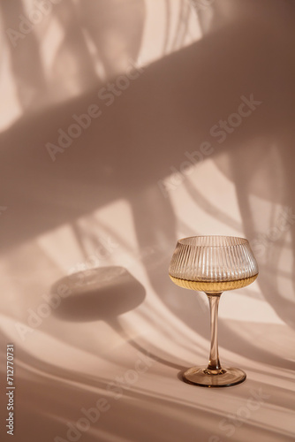 Glass with white wine placed on light background with shadows and fantastic highlights and reflecting bright sunlight in daytime