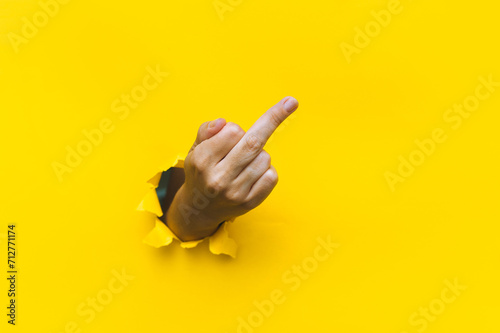 Middle finger of right hand, insulting gesture. Torn hole in yellow paper. Fuck you concept. Aggressive reaction. photo