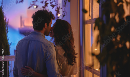 A couple in love stands on the balcony at dusk and enjoys each other's company. Relationship, romance and love concept.