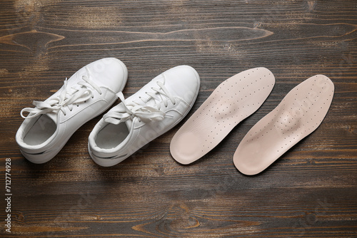 Pair of orthopedic insoles and stylish female shoes on wooden background