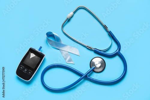 Awareness ribbon with glucometer and stethoscope on blue background. Diabetes concept