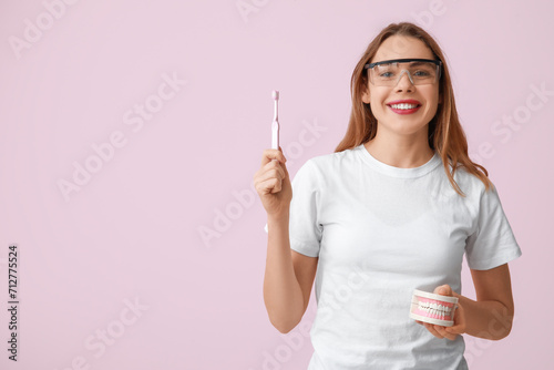 Female dentist with jaw model and toothbrush on pink background. World Dentist Day