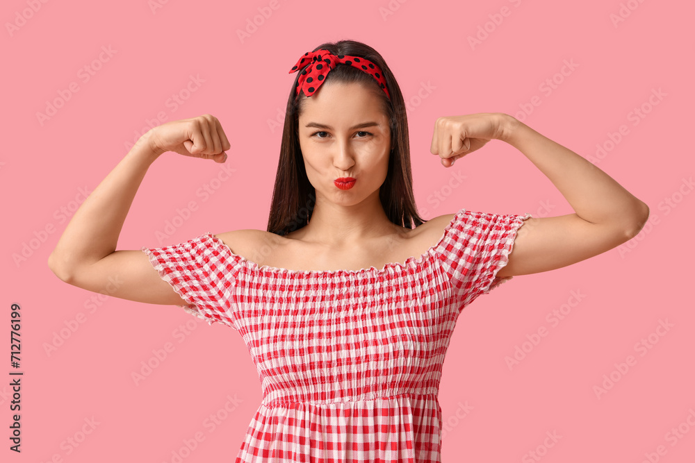 Portrait of strong pin-up woman showing muscles on pink background. Women's History Month Portrait of strong pin-up woman showing muscles on pink background. Women's History Month