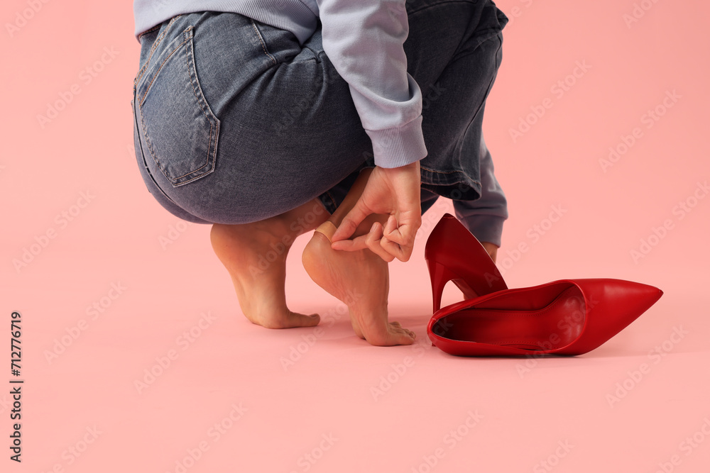Barefoot woman applying plaster on callus against pink background. Uncomfortable shoes concept