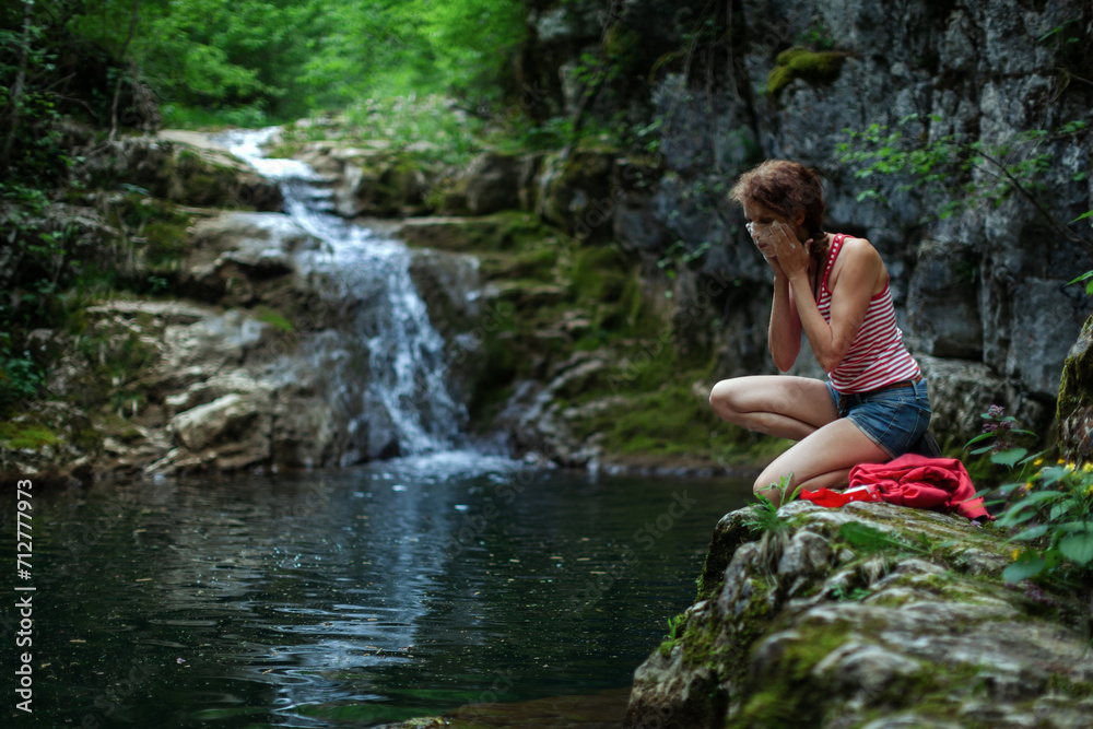 Caucasian Mid Adult Female Adventurer Washing her Face and Taking Care of Her Personal Hygiene in Outdoors Wilderness Caucasian Mid Adult Female Adventurer Washing her Face and Taking Care of Her Personal Hygiene in Outdoors Wilderness