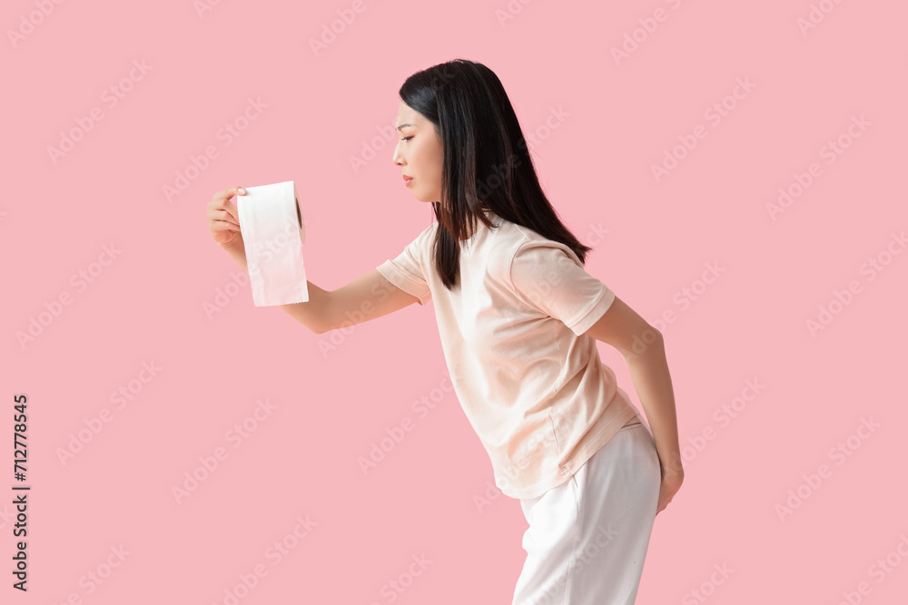 Young Asian woman with hemorrhoids and toilet paper on pink background Young Asian woman with hemorrhoids and toilet paper on pink background