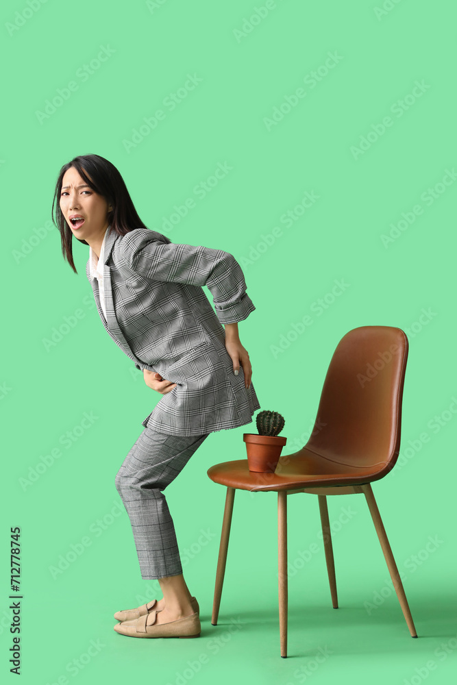 Young Asian businesswoman with hemorrhoids and cactus on chair against green background Young Asian businesswoman with hemorrhoids and cactus on chair against green background
