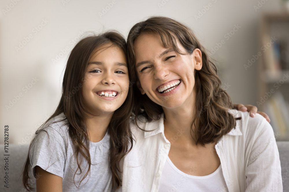 Cheerful embracing loving mom and girl kid head shot portrait. Happy mother and daughter child hugging, looking at camera with toothy smiles, laughing, enjoying family communication Cheerful embracing loving mom and girl kid head shot portrait. Happy mother and daughter child hugging, looking at camera with toothy smiles, laughing, enjoying family communication
