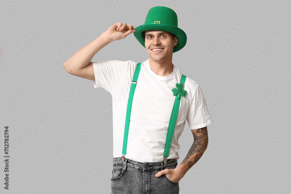 Happy tattooed young man in leprechaun's hat and with shamrock on light background. St. Patrick's Day