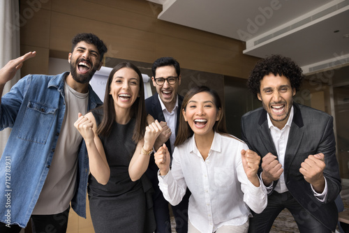 Multiethnic business team of excited project colleagues celebrating teamwork success, successful startup, making winning fist hand gestures, laughing, shouting for joy at camera photo