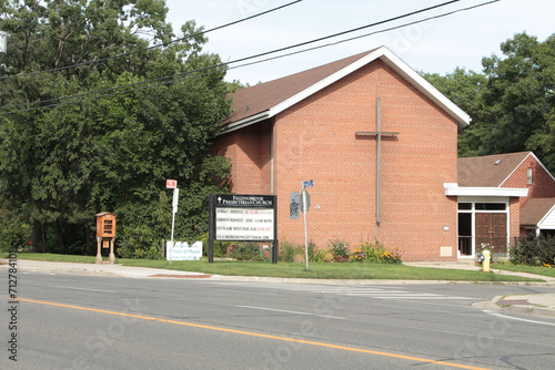 small church chapel next to road with large cross mounted on its side brick wall and tree next to it photo