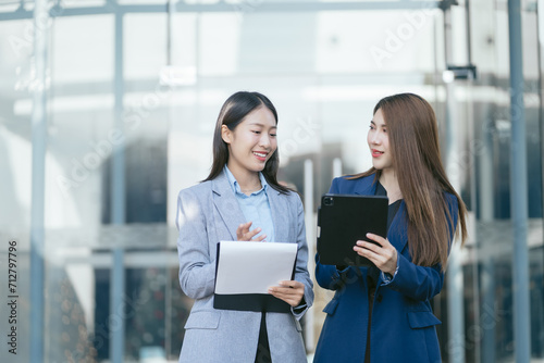 Portrait of two stylish pretty women standing and holding laptop and mobile phones.