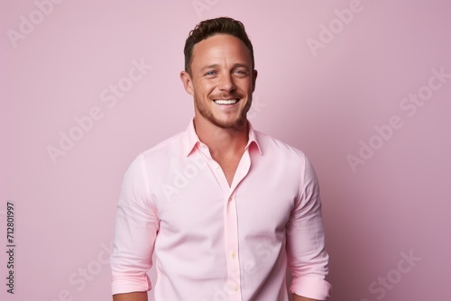 Handsome young man in pink shirt is looking at camera and smiling while standing against pink background