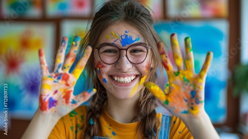Smiling beautiful young woman playing with colors  paint on hands and face  showing the two hands full of colorful pigment to the camera  concept of art and creativity.