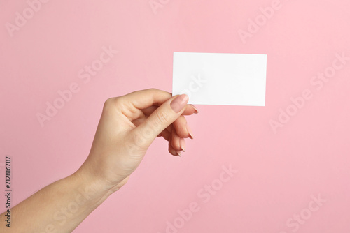 Woman holding blank business card on pink background, closeup. Mockup for design