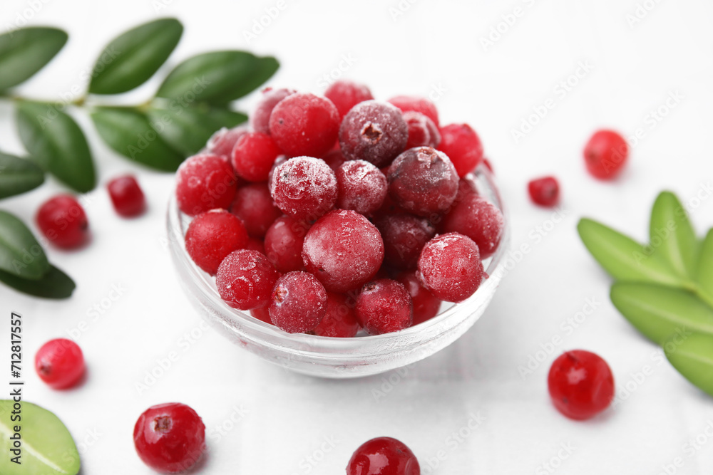 Frozen red cranberries in bowl and green leaves on white tiled table, closeup Frozen red cranberries in bowl and green leaves on white tiled table, closeup