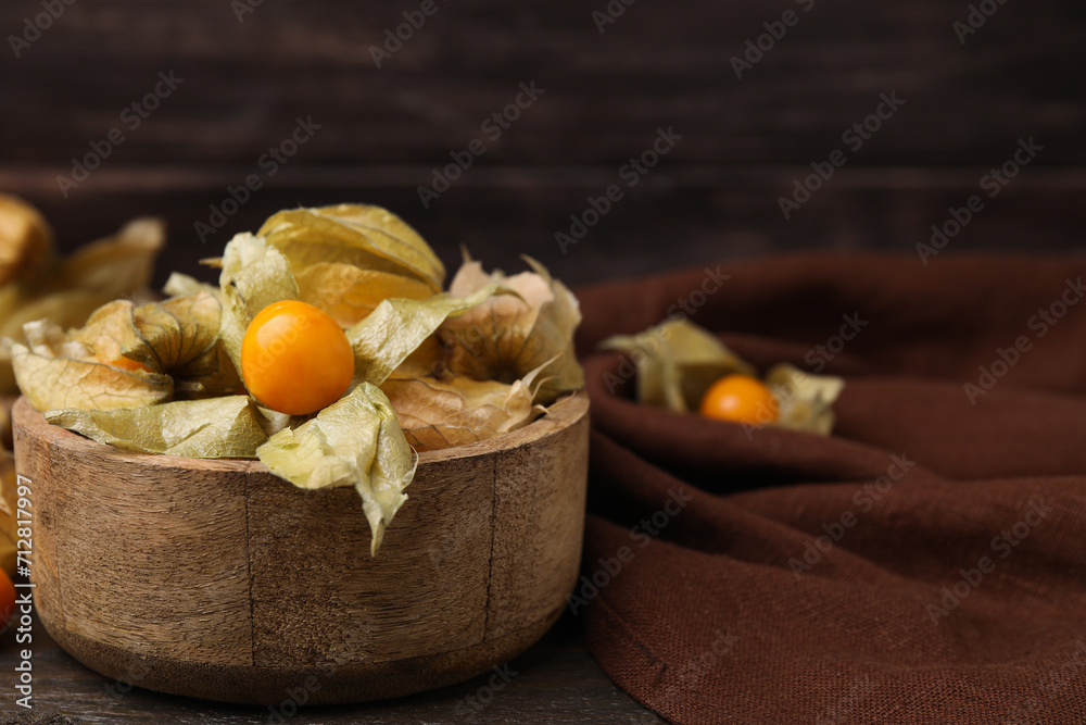 Ripe physalis fruits with calyxes in bowl on wooden table, space for text Ripe physalis fruits with calyxes in bowl on wooden table, space for text