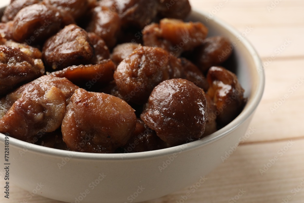 Roasted edible sweet chestnuts in bowl on light wooden table, closeup Roasted edible sweet chestnuts in bowl on light wooden table, closeup