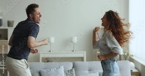 Happy cheerful active young couple dancing to disco music at home party, having fun, laughing, singing songs, enjoying activity, leisure, motion, entertainment together, celebrating mortgage photo