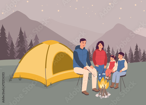 Smiling Family With Two Little Children In Puffer Vest Sitting In Front Of Tent Roasting Marshmallows Over A Campfire. Full Length.