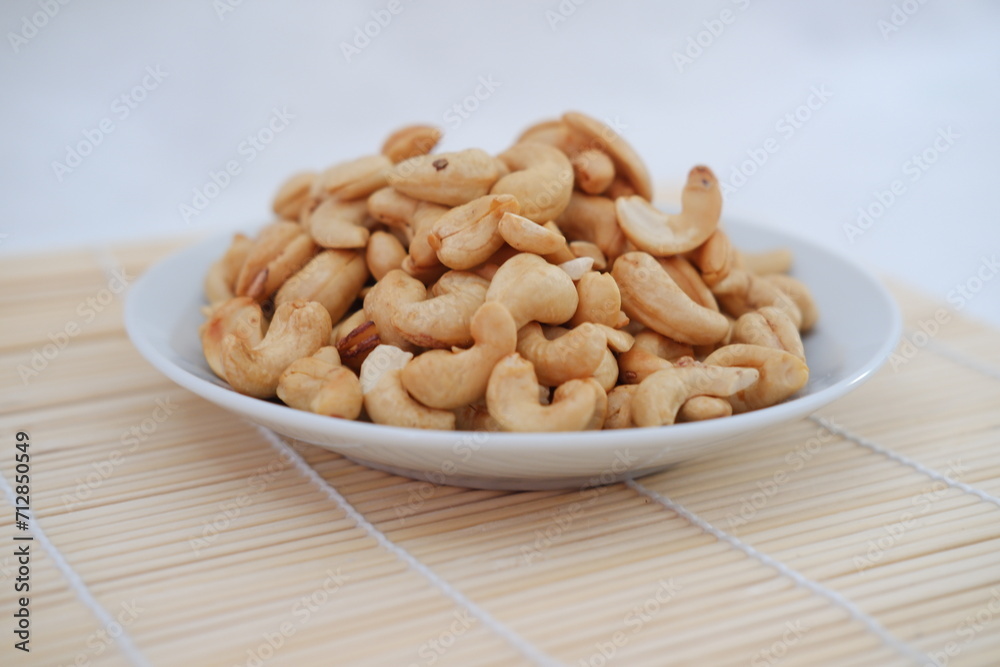 Roasted cashew nuts in white bowl on bamboo mat, stock photo Roasted cashew nuts in white bowl on bamboo mat, stock photo