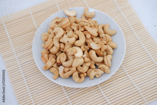 Roasted cashew nuts in white bowl on bamboo mat, stock photo