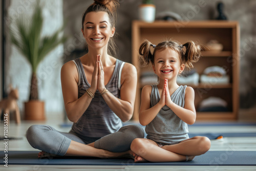 Parent and her charming little daughter are smiling while doing yoga together at home