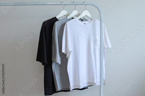 Three color black white gray mockup tees hanging on a clothing rack against grey cement background. 